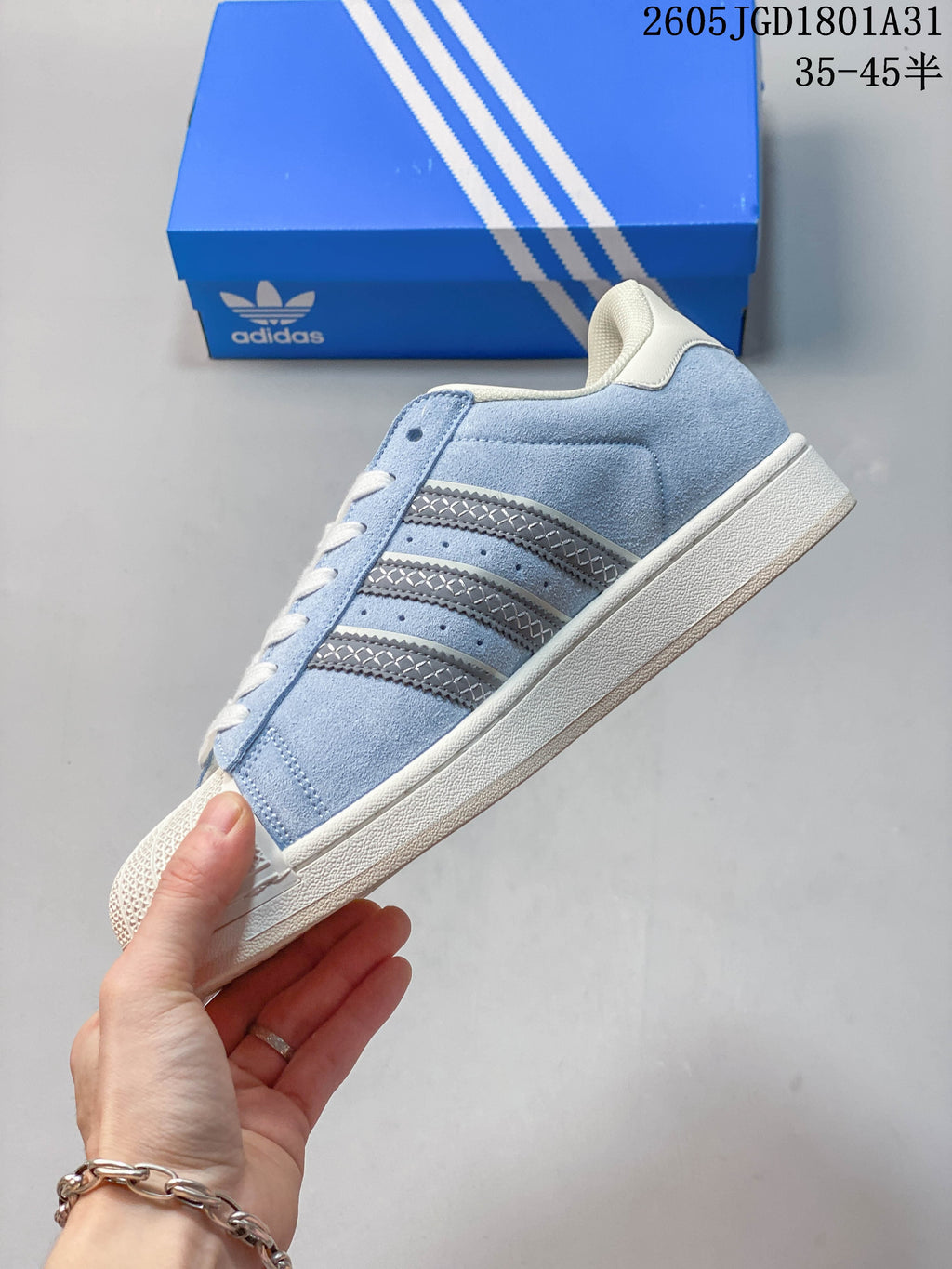 Side view showing the light blue upper, silver stripes, cream sole, and shell toe.