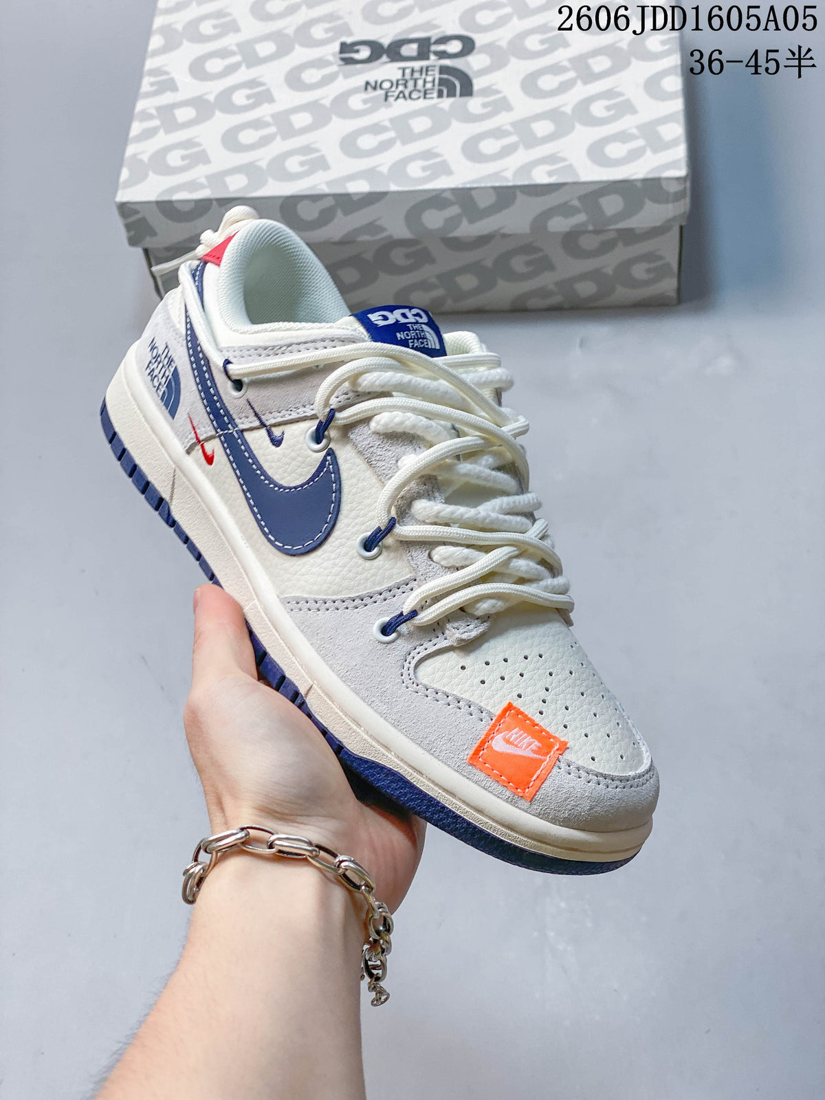 Angled view of an off-white Nike SB Dunk Low with navy accents, orange toe detail, and rope-style laces.