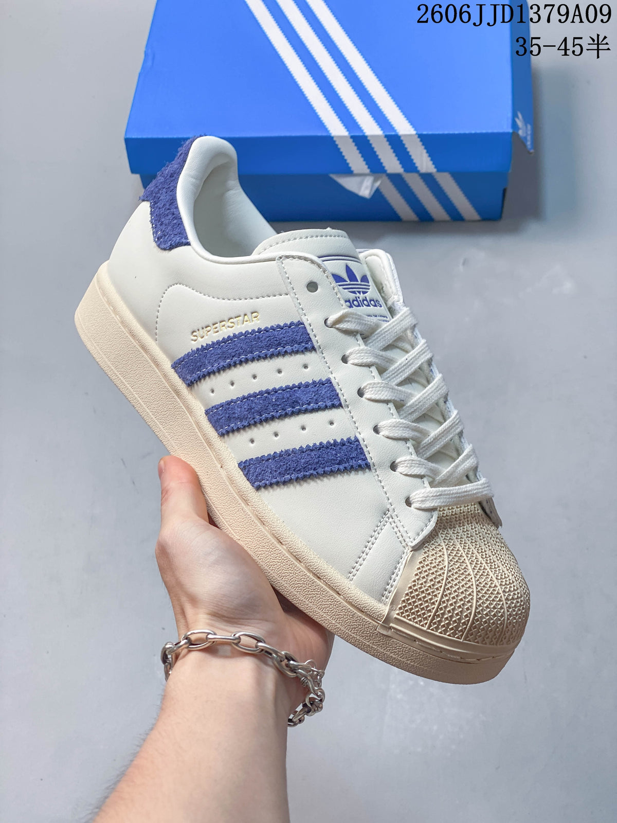 Side view of a cream adidas Superstar sneaker with blue stripes, a shell toe and a tonal sole.