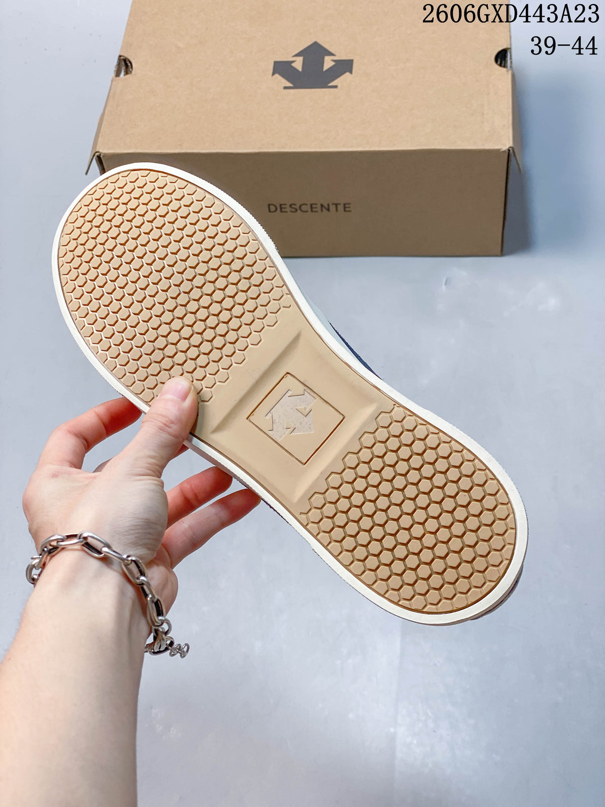 Bottom view of the sneaker showing a tan honeycomb-patterned outsole and a DESCENTE shoe box.