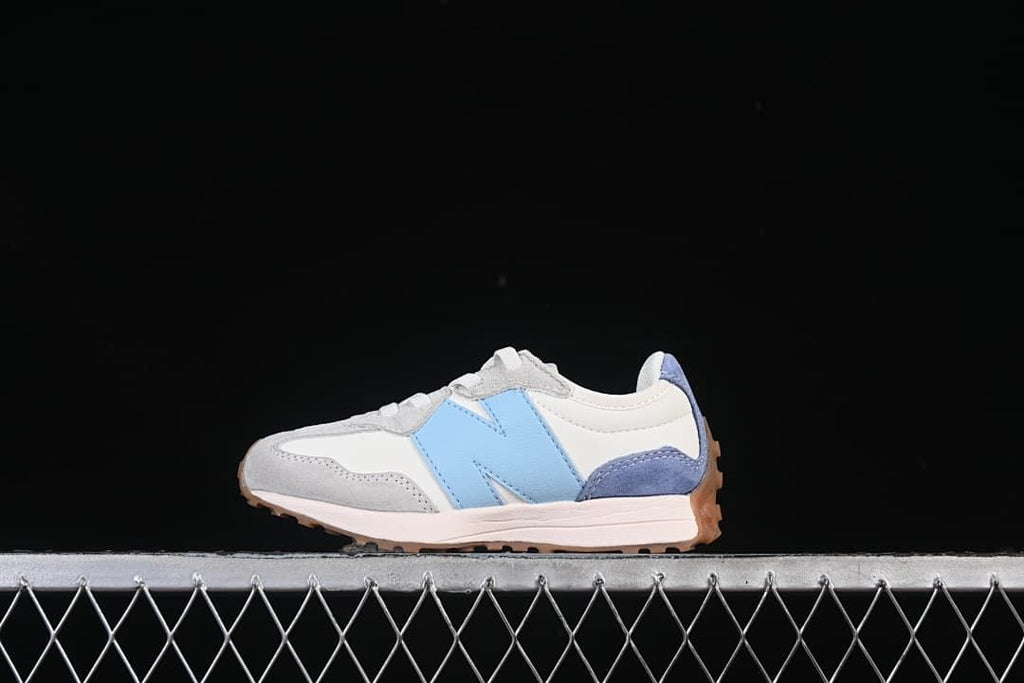 Side view of a white, light blue, and grey New Balance kids sneaker with a gum-colored outsole.