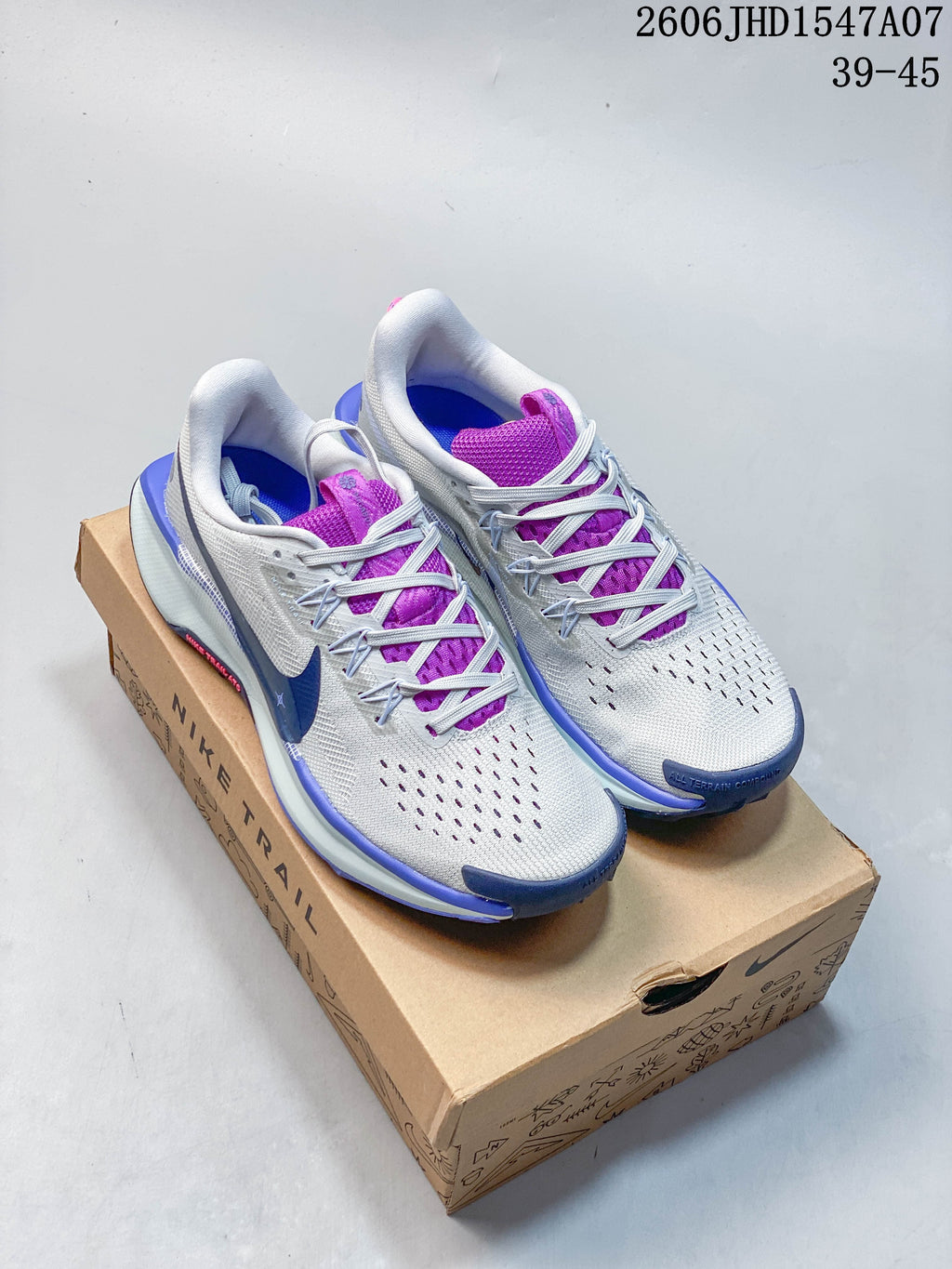 Pair of gray Nike ReactX Pegasus Trail 5 trail running shoes with purple and blue details, shown on a Nike Trail box.