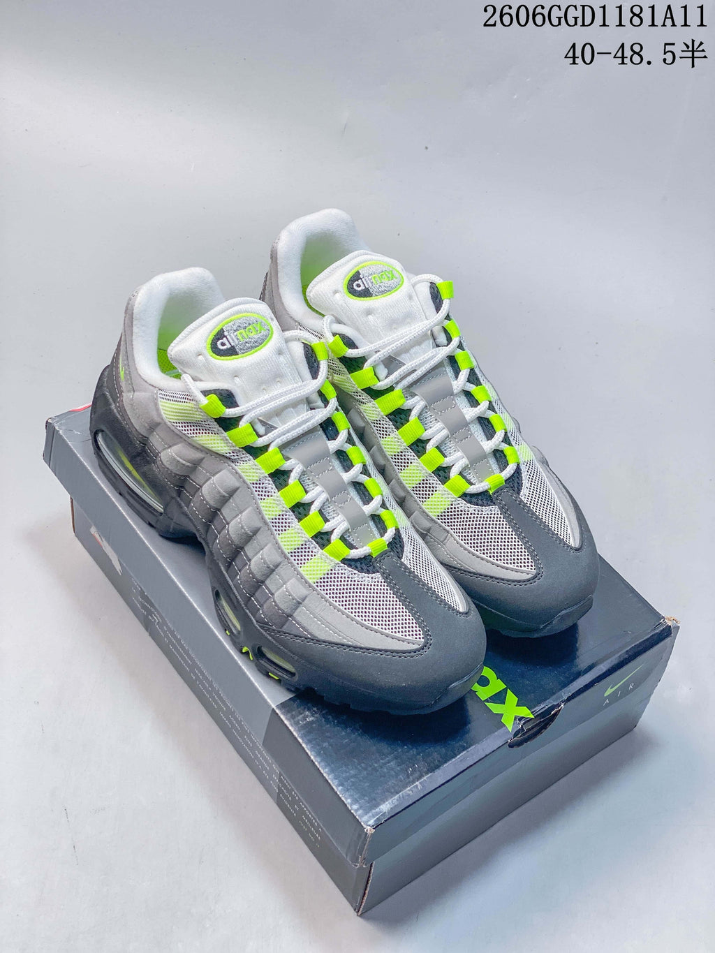 Pair of grey Nike Air Max 95 OG sneakers with white mesh and volt accents, shown on the shoebox.
