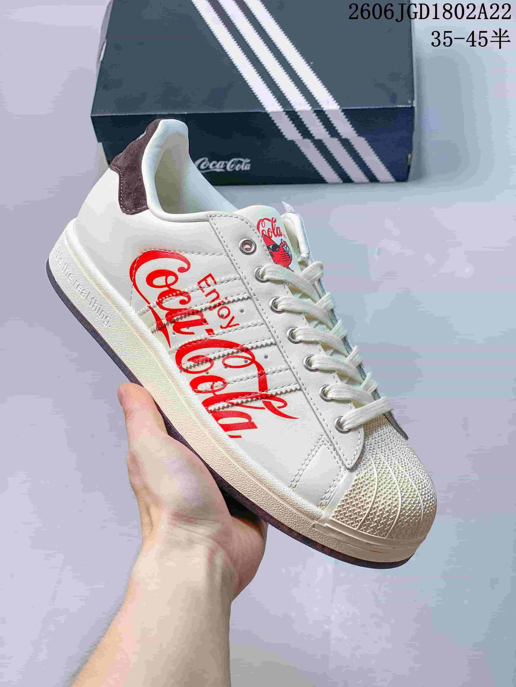 Close-up of an off-white low-top sneaker with red Coca-Cola side graphics, laces, and a textured shell toe.