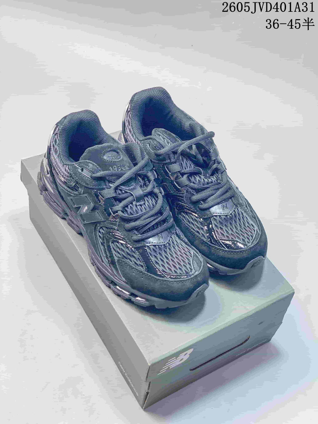 Pair of charcoal gray New Balance 997 sneakers on a shoe box, with code 2605JVD401A31 and size range text visible.