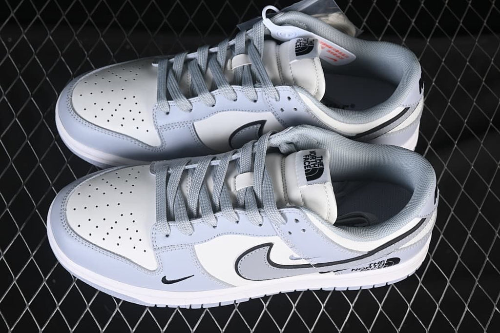 Top view of a pair of white and light gray low-top sneakers with gray laces and North Face tongue graphics