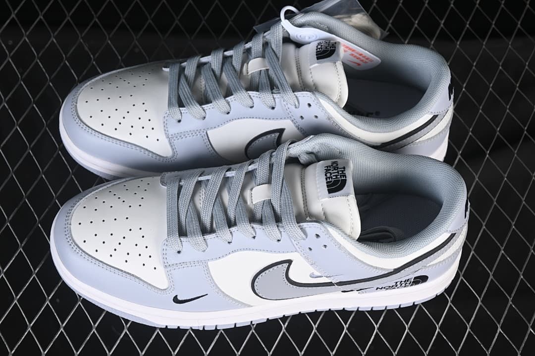 Top view of a pair of white and light gray low-top sneakers with gray laces and North Face tongue graphics