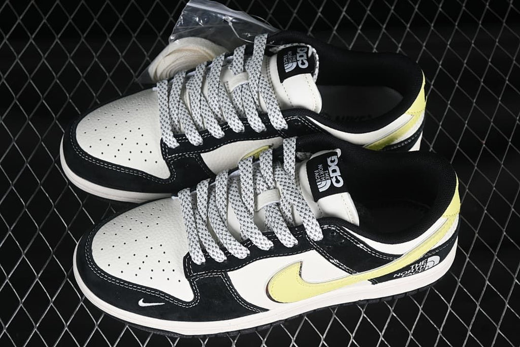 Pair of black and white low-top sneakers with pale yellow accents, patterned laces, and branded tongues.