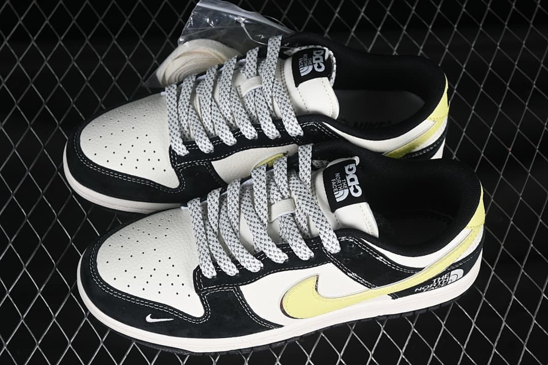 Pair of black and white low-top sneakers with pale yellow accents, patterned laces, and branded tongues.