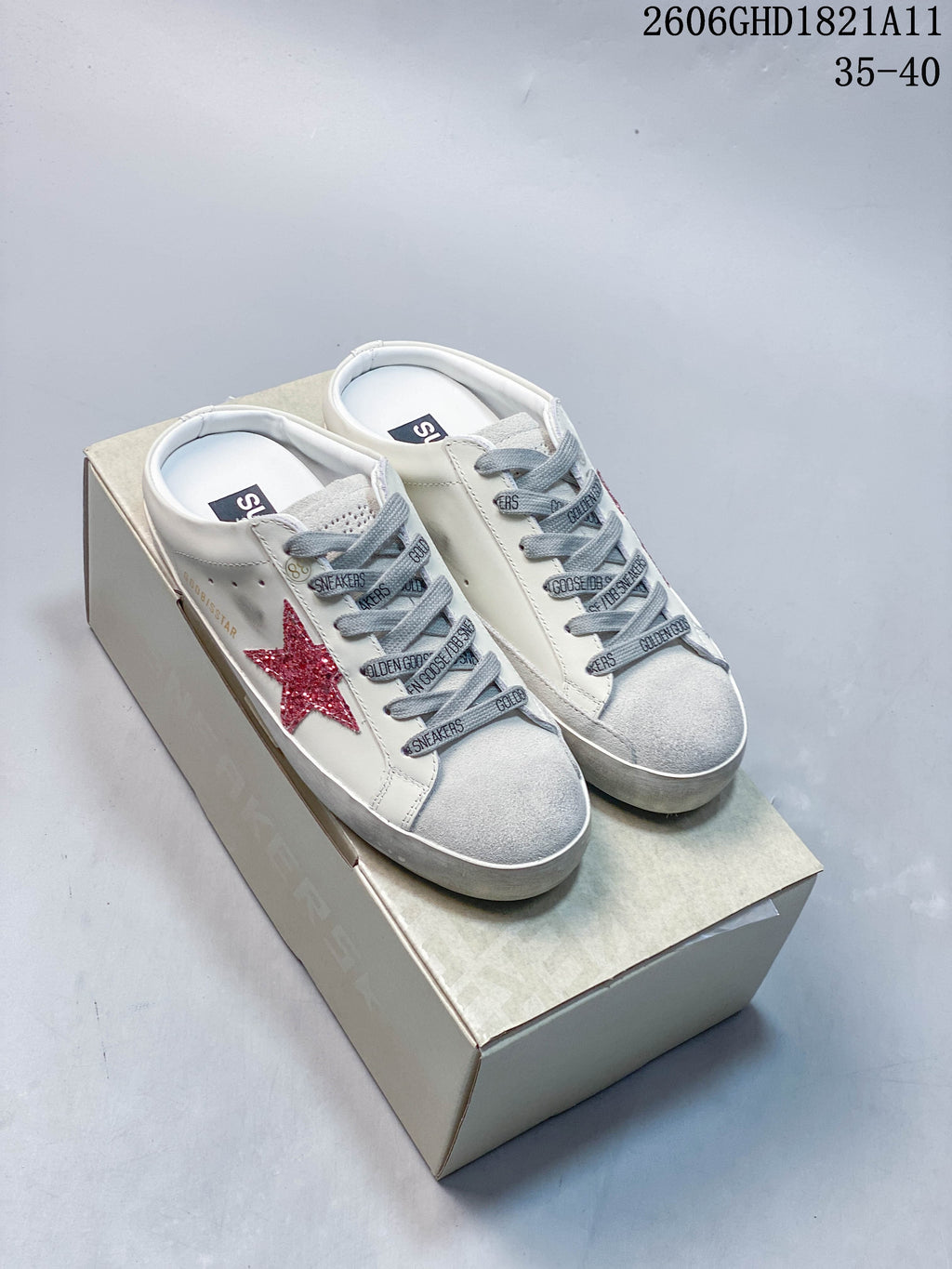 Pair of white Golden Goose Super-Star low-top sneakers with red glitter stars, gray laces, and gray toe panels on a box.