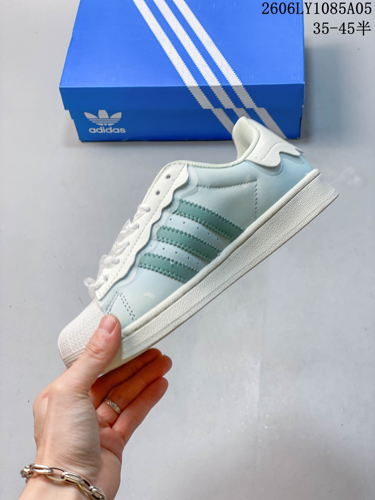 Side view of the pale blue Superstar sneaker with three stripes, scalloped overlays, and a shell toe.