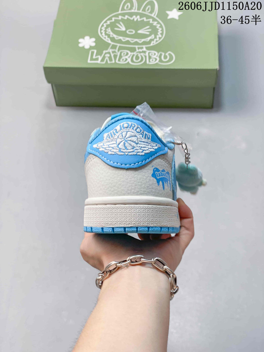 Rear view of a white and blue sneaker showing a wing-style heel emblem and a dangling plush charm.