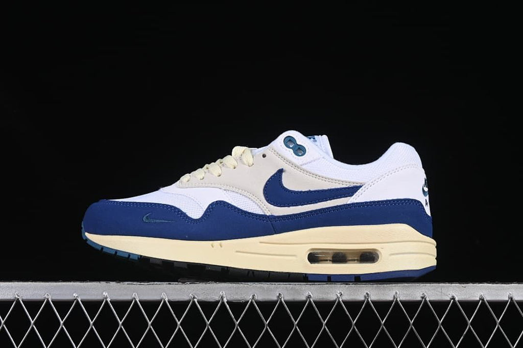Side view of white, navy and cream Nike Air Max 1 sneakers