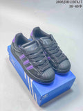 Pair of charcoal-black adidas Superstar ST sneakers with purple accents and shell toes, shown on a blue shoebox