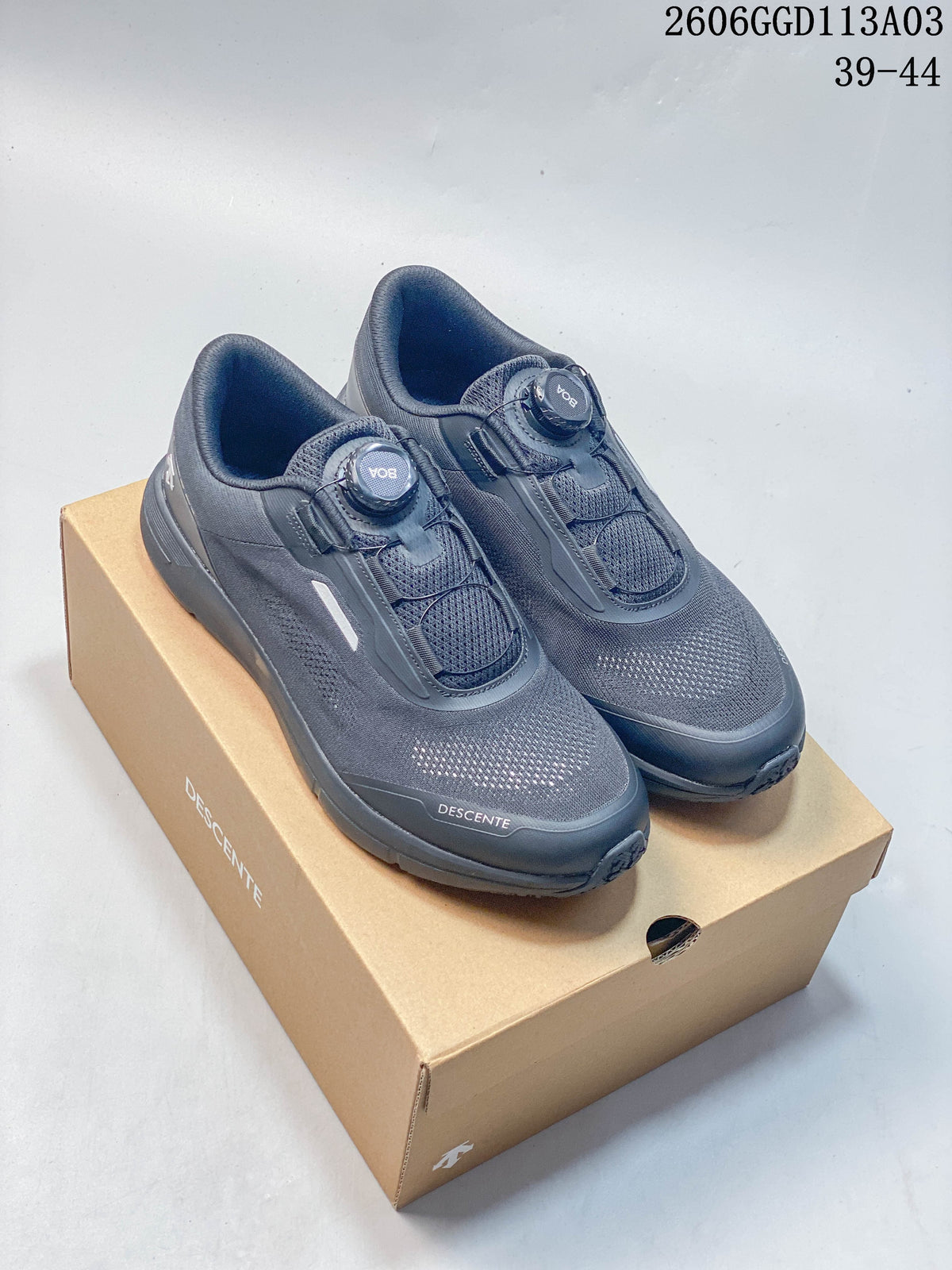 Pair of gray DESCENTE low-top shoes with dial closures, shown on a branded box