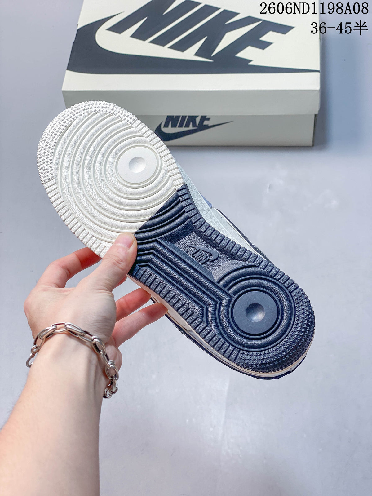 Close-up of the sneaker outsole showing off-white and dark blue tread sections, with the shoe box in the background; image overlay shows code 2606ND1198A08 and size range 36–45.5.