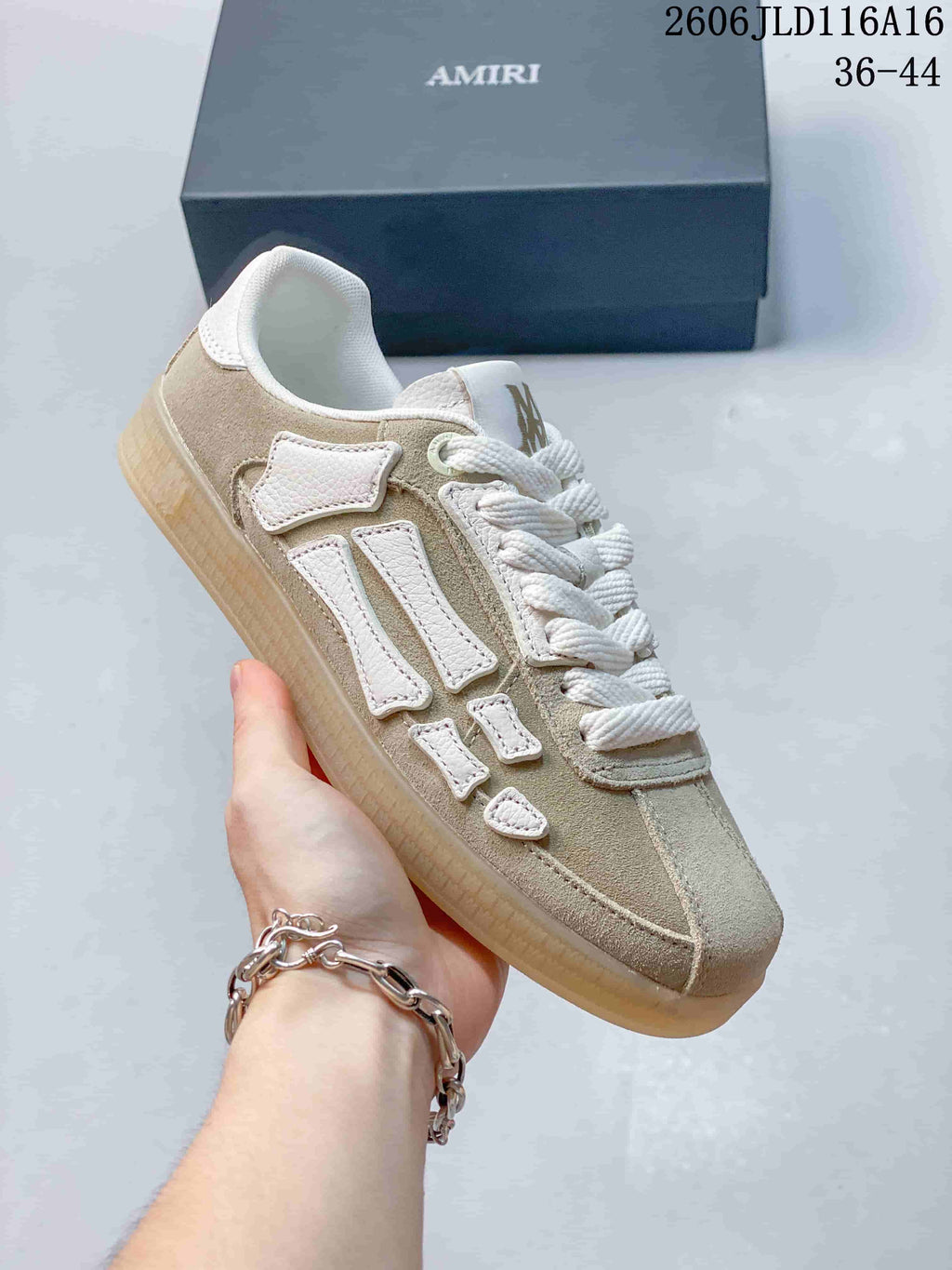 Angled close-up of the beige-toned sneaker with white laces and bone-shaped side appliqués.