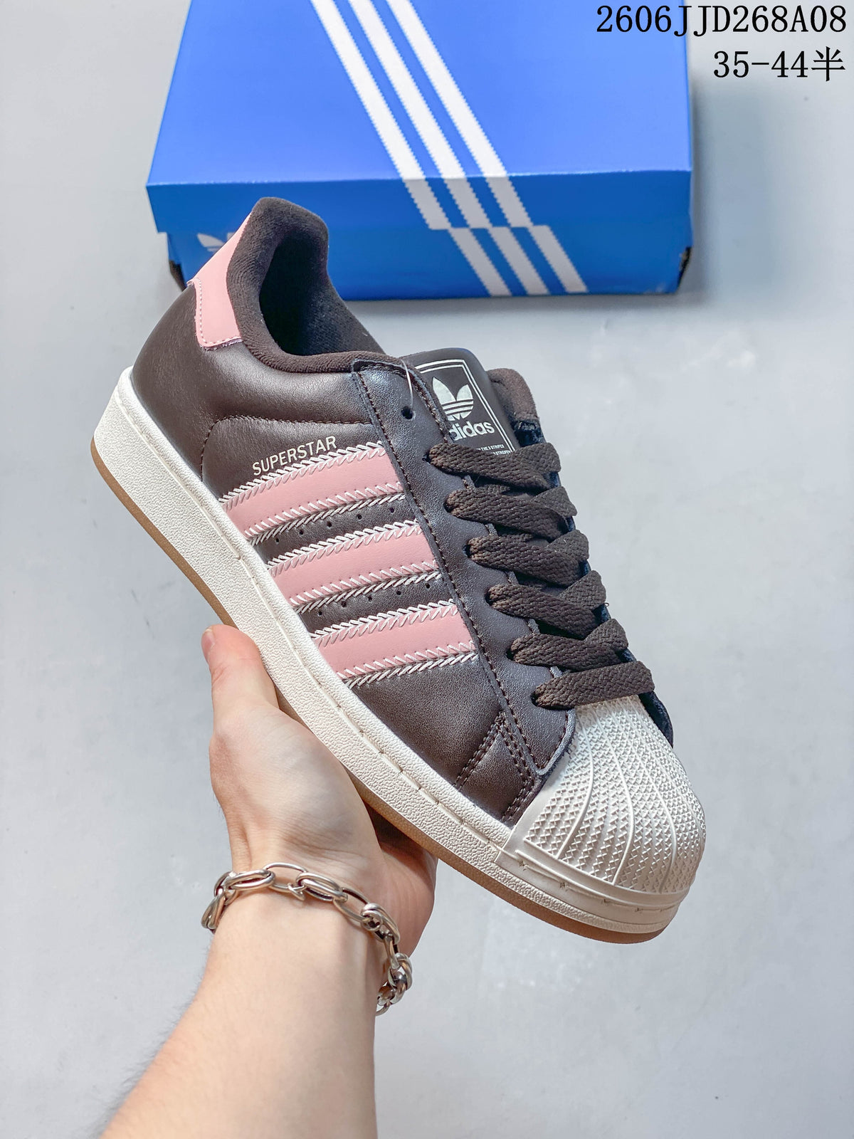 Side view of a dark brown Superstar 2 sneaker with pink stripes and a light shell toe.