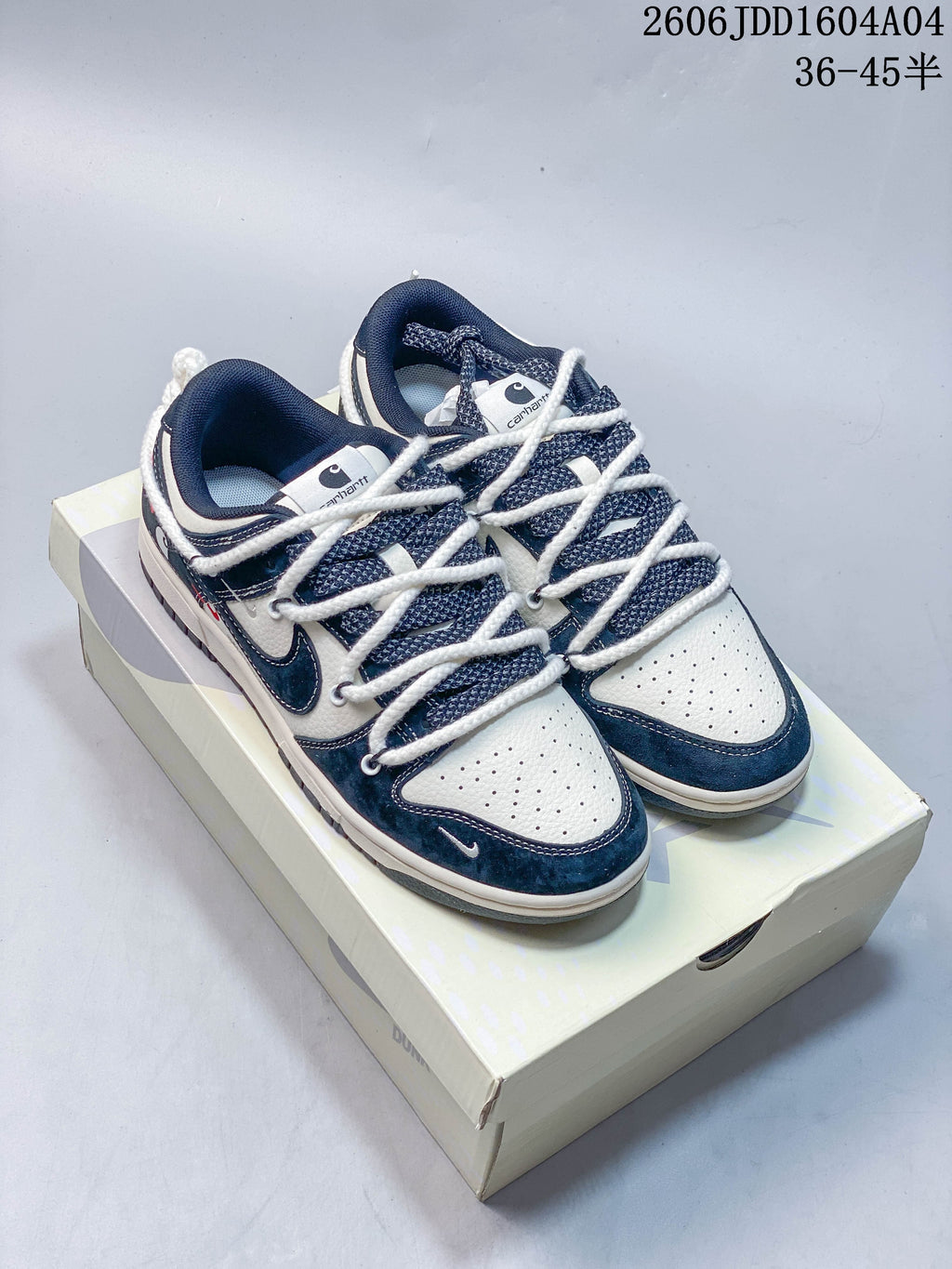 Pair of white and navy blue low-top sneakers with thick white laces, shown on a Nike Dunk box.