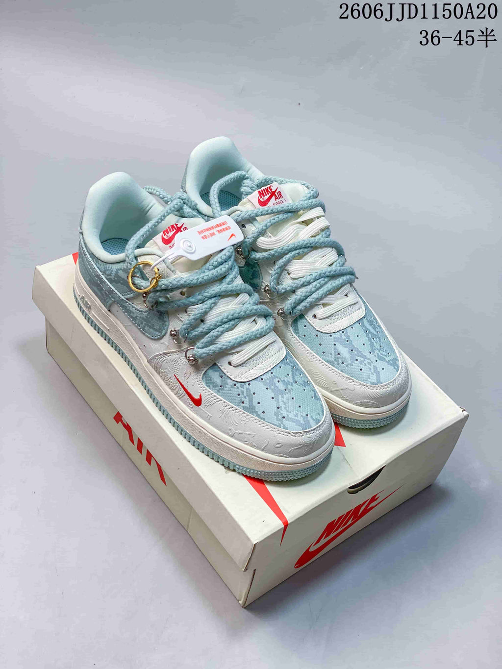 Pair of pale blue and white low-top sneakers with patterned panels, rope-style laces, decorative hardware, and a matching shoe box