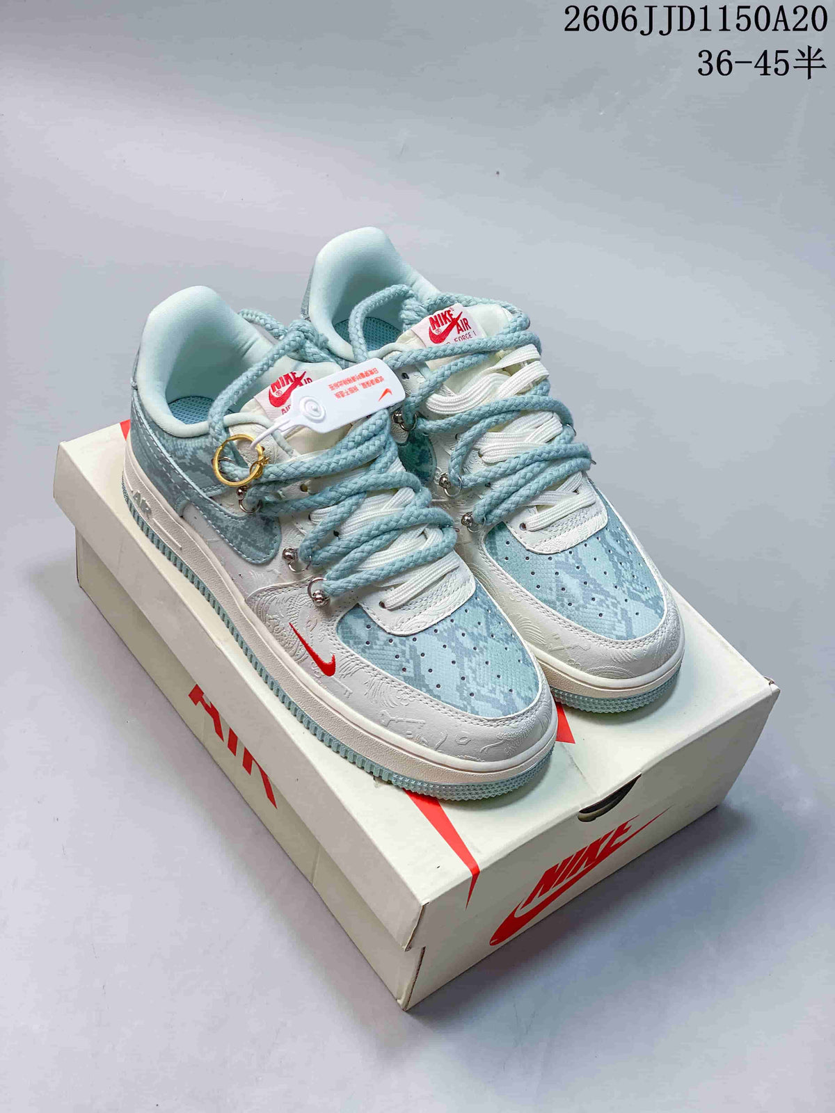Pair of pale blue and white low-top sneakers with patterned panels, rope-style laces, decorative hardware, and a matching shoe box