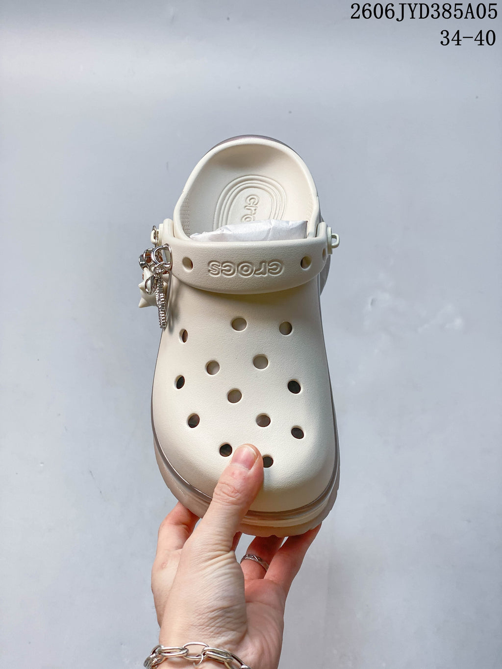 Top view of an ivory perforated clog with decorative charms on the strap