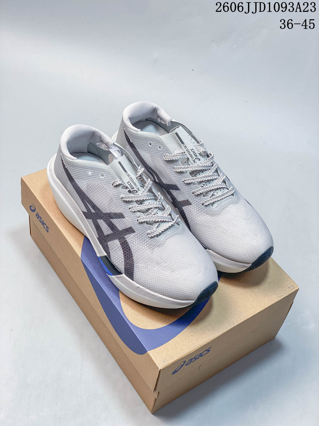 Light gray ASICS running shoes with dark side logos, photographed on a shoebox