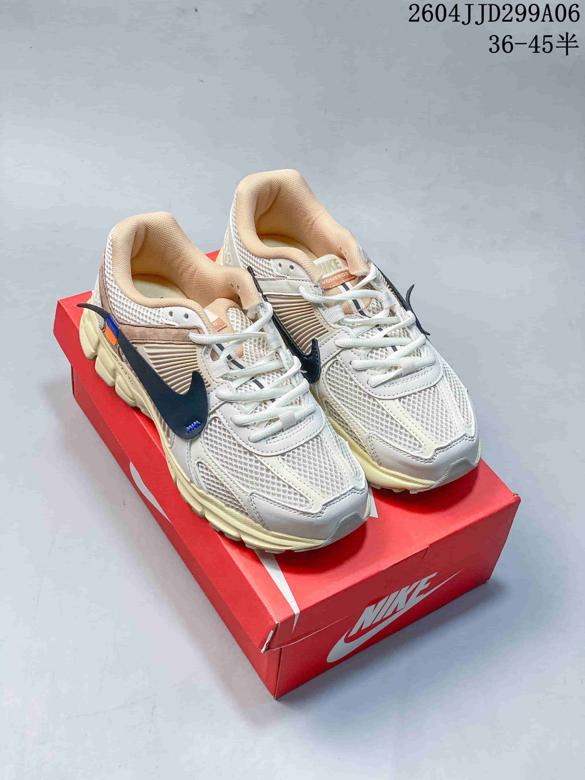 Light-colored Nike Zoom Vomero 5 sneakers with dark accents, shown from above on a red shoe box.