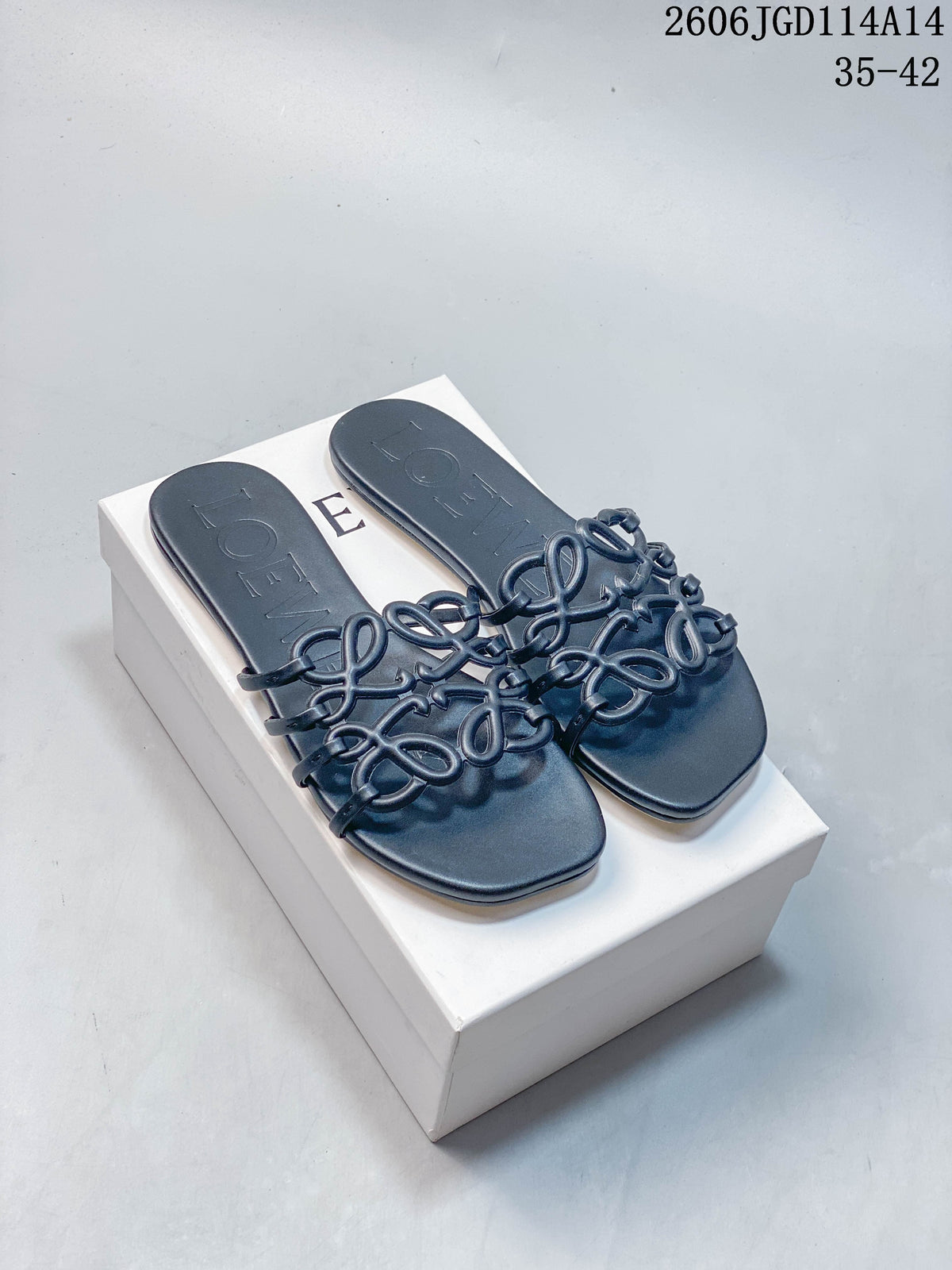 Pair of dark navy flat slide sandals with sculptural Anagram-style straps, displayed on a white box.