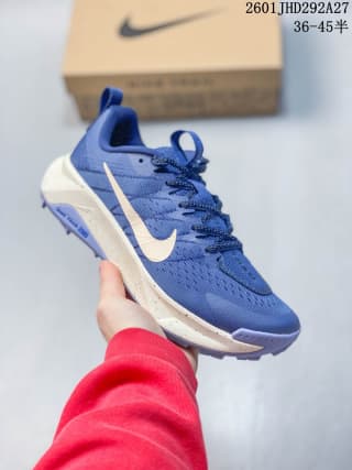 Blue Nike trail running shoe held in front of a Nike shoe box, with a white Swoosh and contrasting midsole details.