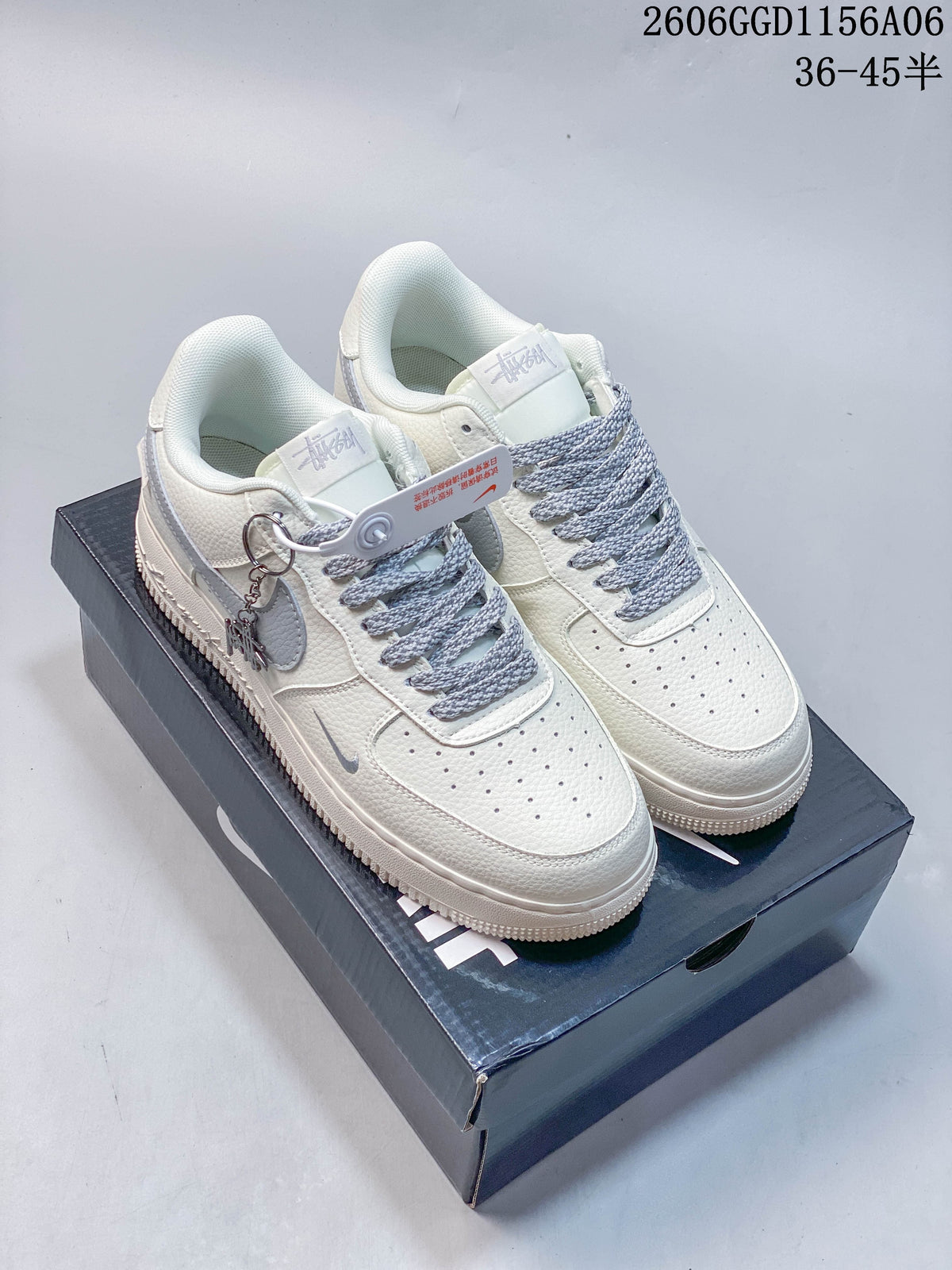 Pair of ivory and grey Nike Air Force 1 sneakers with rope-style laces and decorative side charms