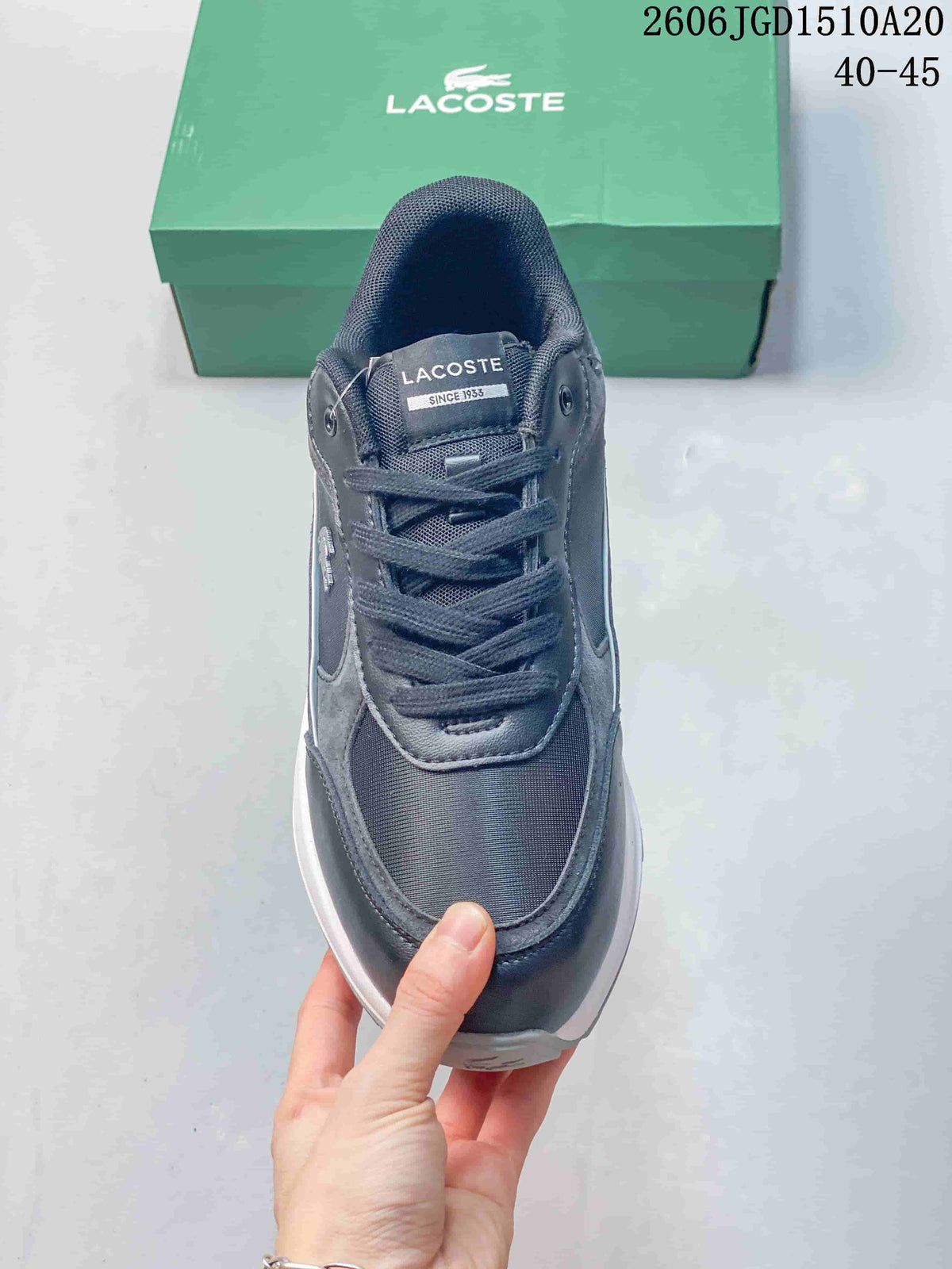 Front view of a grey and navy lace-up sneaker with a Lacoste tongue label.