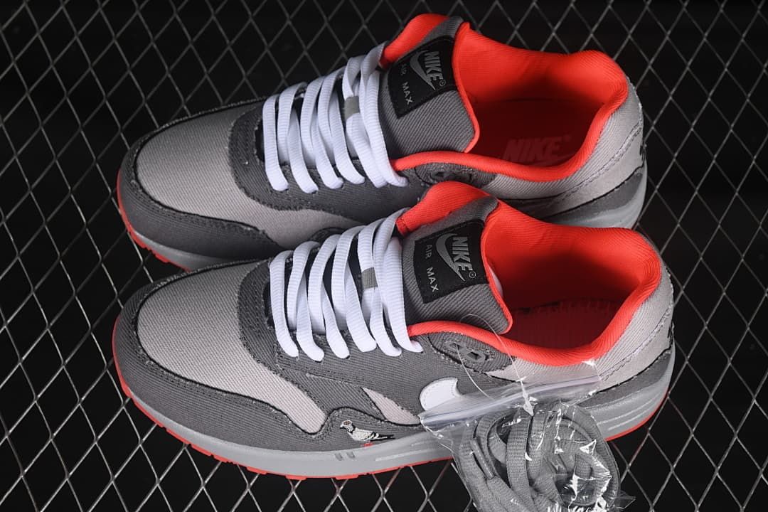 Pair of grey and crimson Nike Air Max 1 sneakers with an additional set of grey laces pictured.