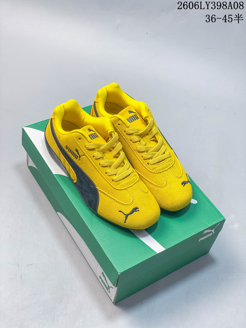 Yellow PUMA Speedcat OG sneakers with dark side stripes on a green shoe box