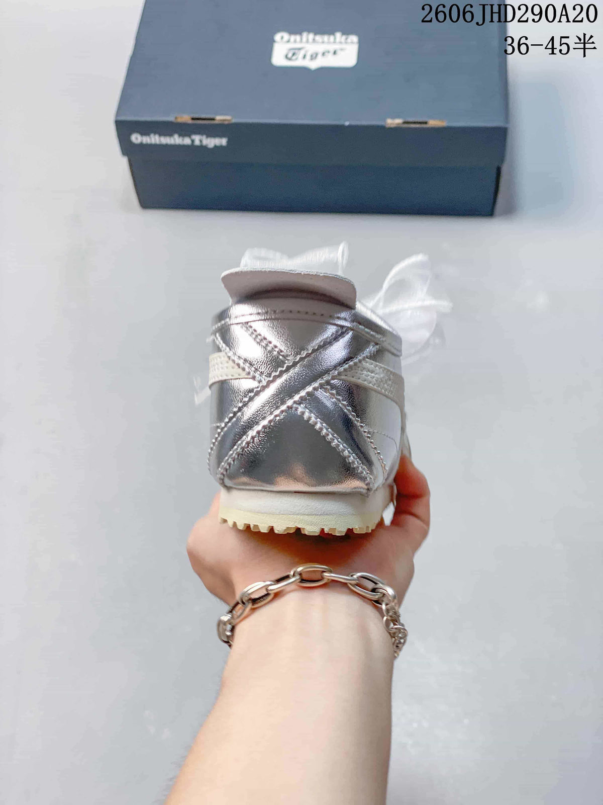 Rear view of a silver sneaker with cream trim and ribbon laces