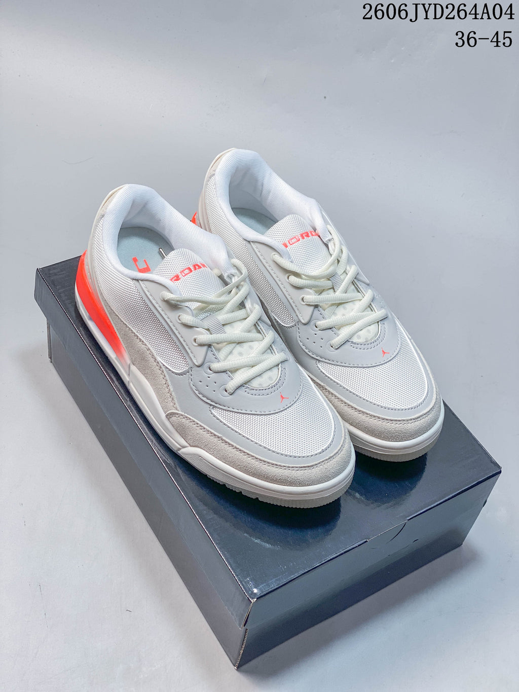 Pair of sail and gray Jordan low-top sneakers with red-orange accents on a dark shoebox