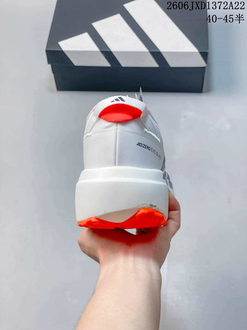 Rear view of a white shoe with an orange heel accent and thick white midsole.