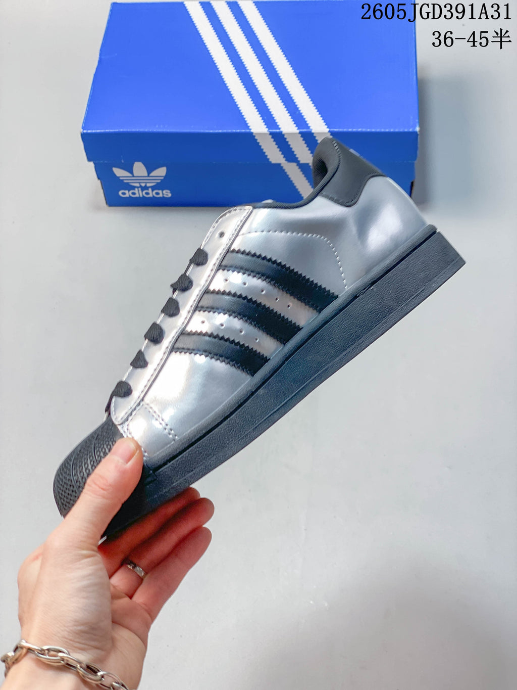 Side view of a silver Superstar sneaker with dark stripes and a dark sole.
