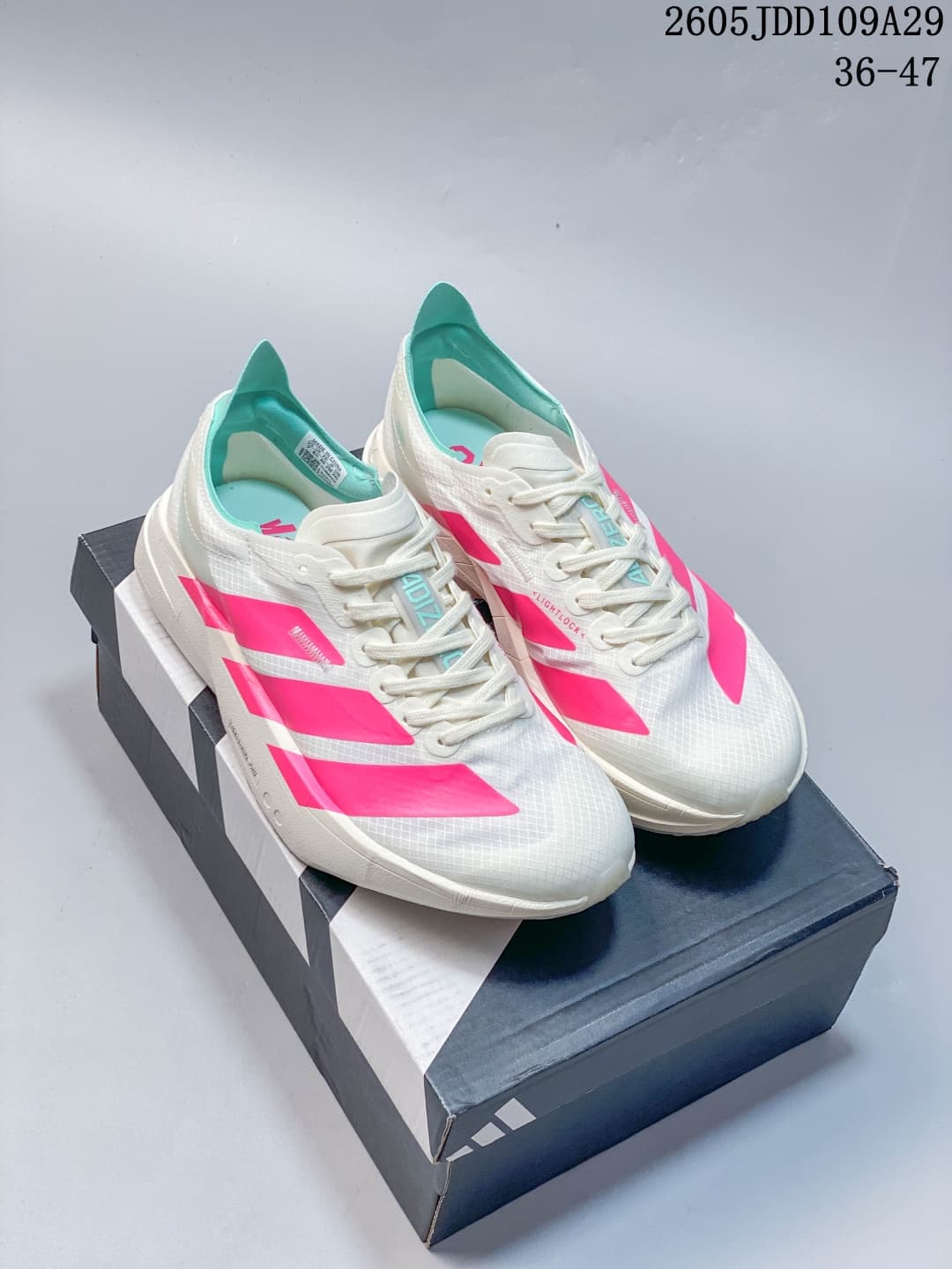 Pair of white Adidas Adizero Adios Pro 4 sneakers with bright pink side details and teal lining displayed on a shoebox.