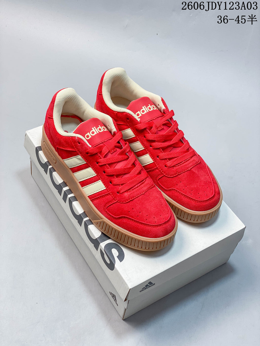 Pair of red Adidas Originals D-PAD Classic sneakers with off-white stripes and gum-colored soles on a shoe box