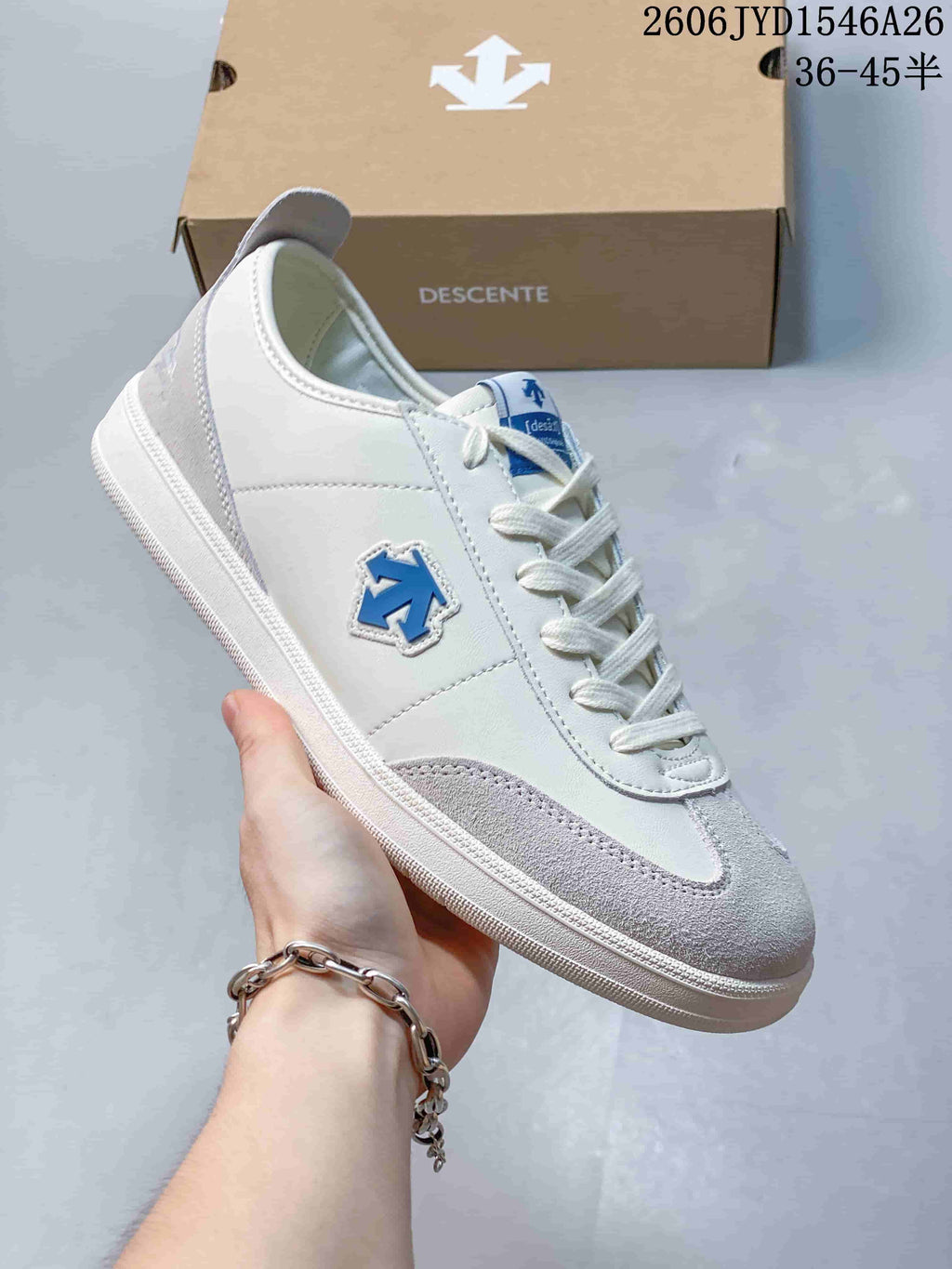 Close-up of a white and light gray Descente low-top sneaker with a blue side emblem.