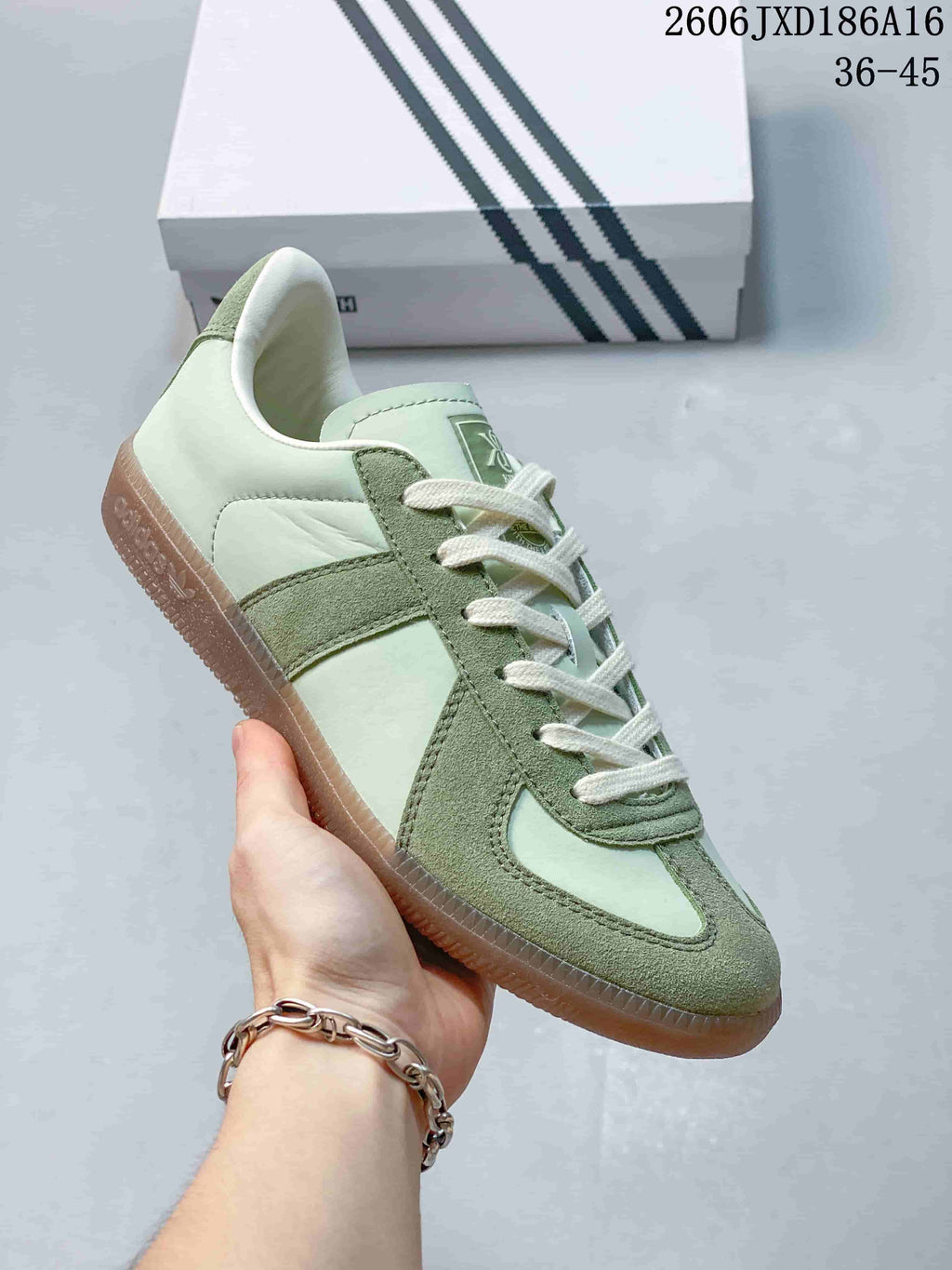 Close view of a pale green and darker green low-top sneaker with cream laces and a gum-colored sole.