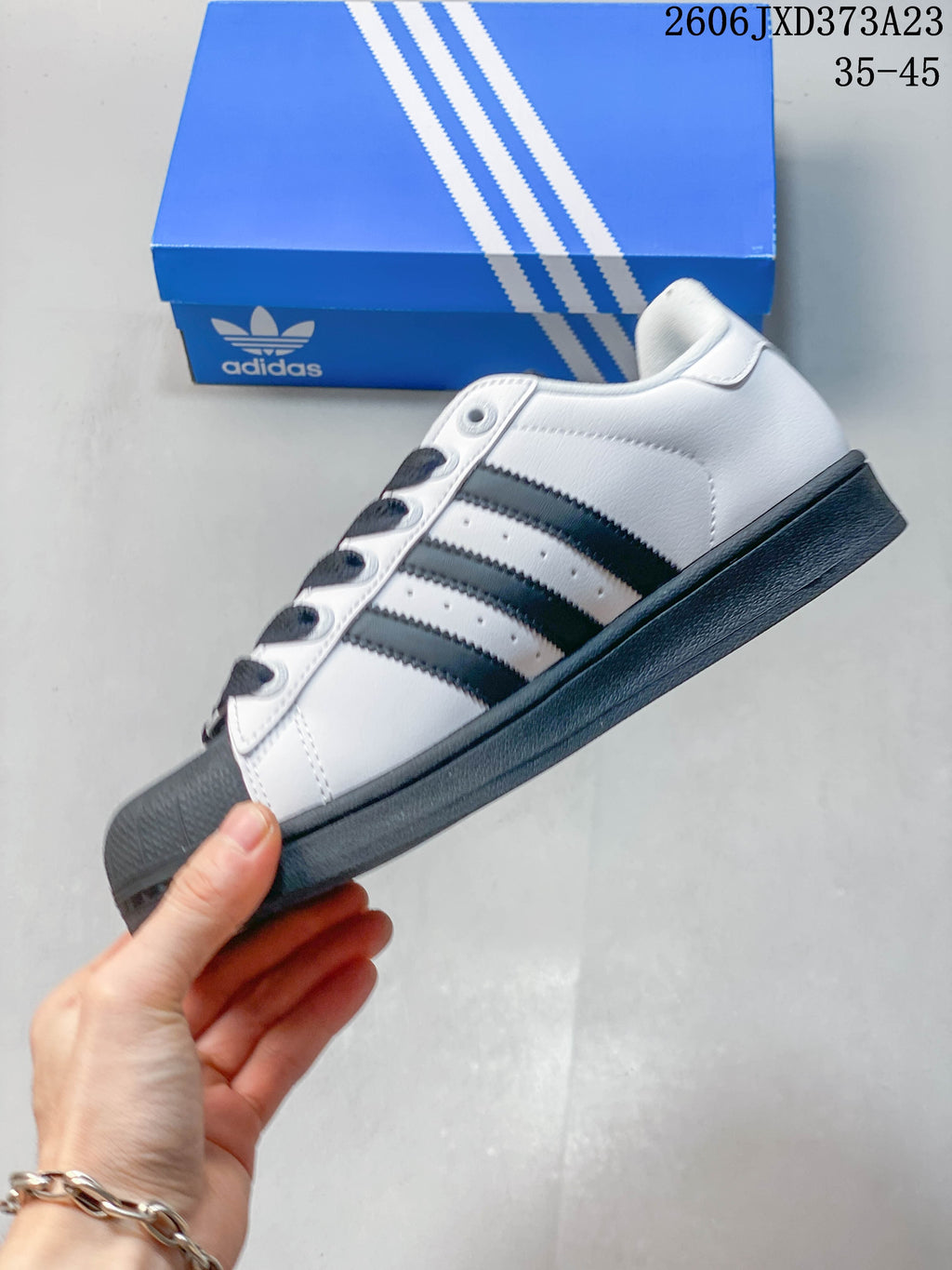 Side profile of a white Superstar sneaker with dark three-stripe detailing and a shell toe.