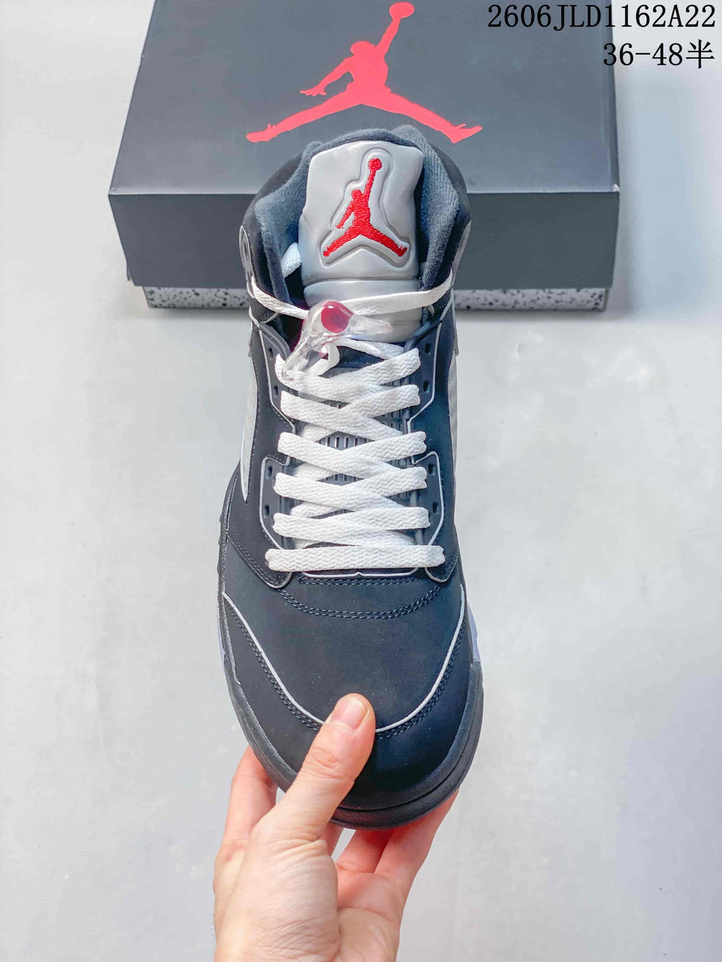 Front view of a dark high-top sneaker with white laces and a red embroidered tongue logo.