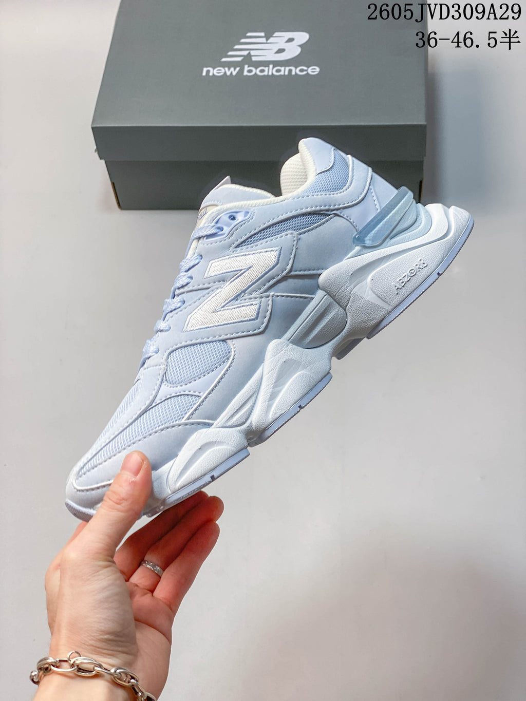 Side profile of a pale blue and white New Balance 9060 sneaker with mesh panels and a large side logo.