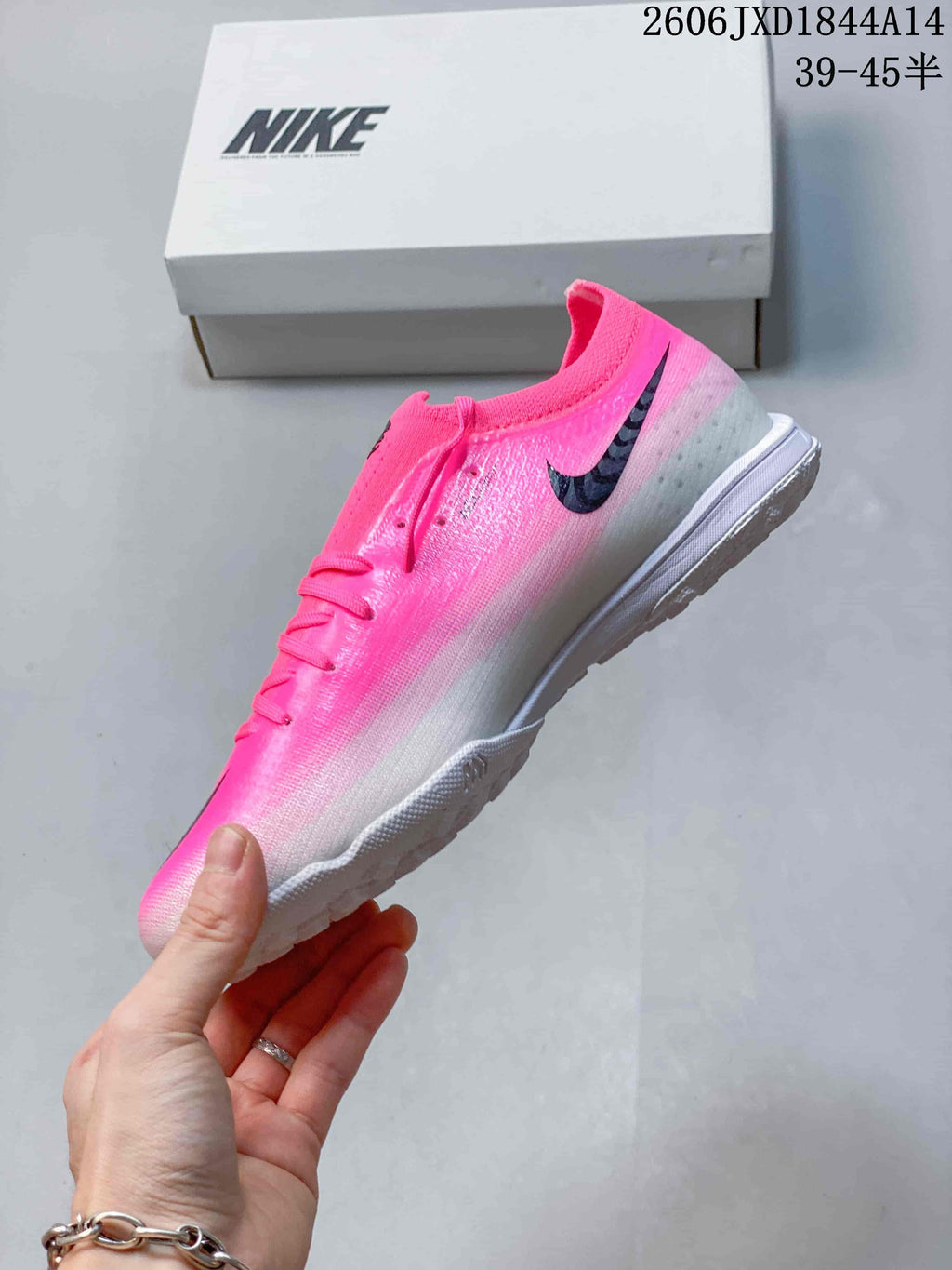 Side view showing the pink-to-gray gradient and black Swoosh on a Nike soccer cleat.
