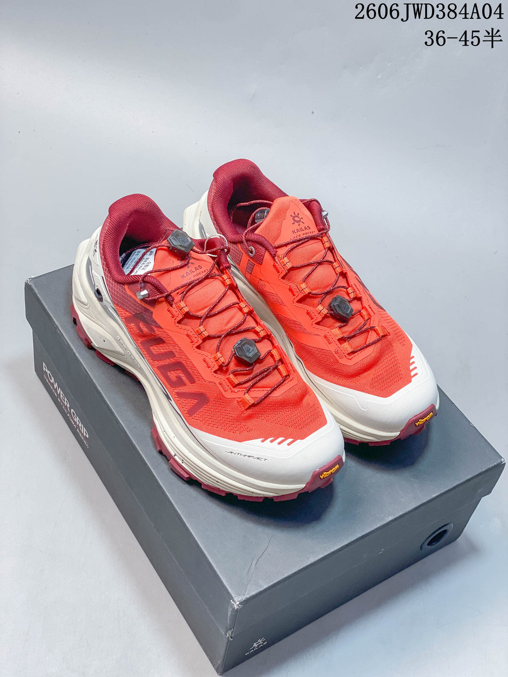 Pair of coral-orange KAILAS FUGA EX3 trail shoes on a shoe box; dial-adjustable laces and burgundy trim are visible.