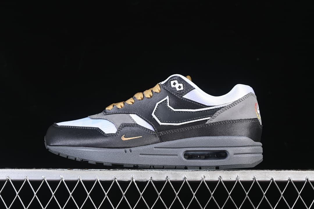 Side view of a black, grey, and white Nike Air Max 1 sneaker with gold-tone details