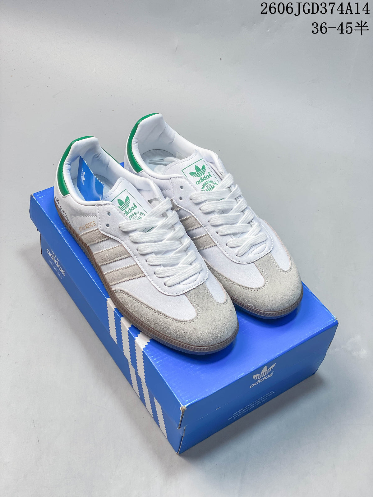 Pair of white Adidas Originals Samba-style low-top sneakers with gray overlays, green heel accents, and gum-colored soles.