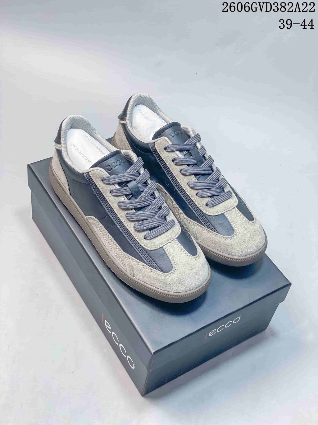 Gray and dark blue ECCO low-top lace-up sneakers with contrast panels, shown on a shoe box.